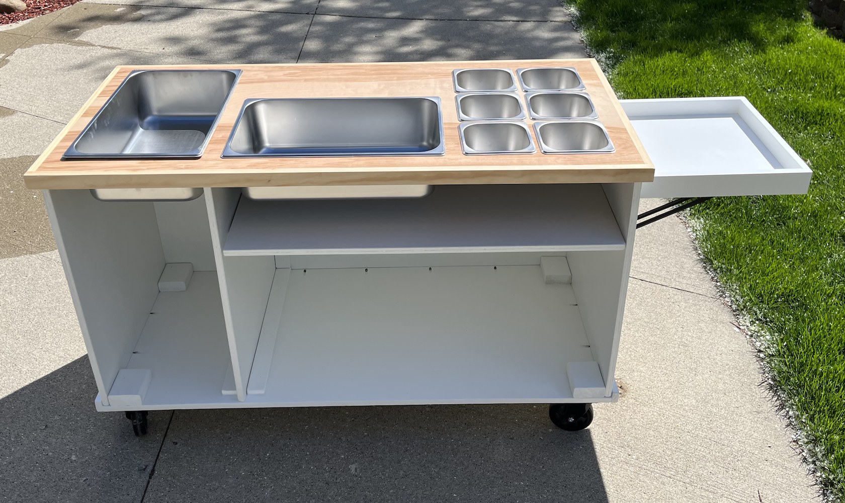 Candy and dessert cart with a natural wood top, customizable-size stainless pan inserts, a fold-out tray and open storage below