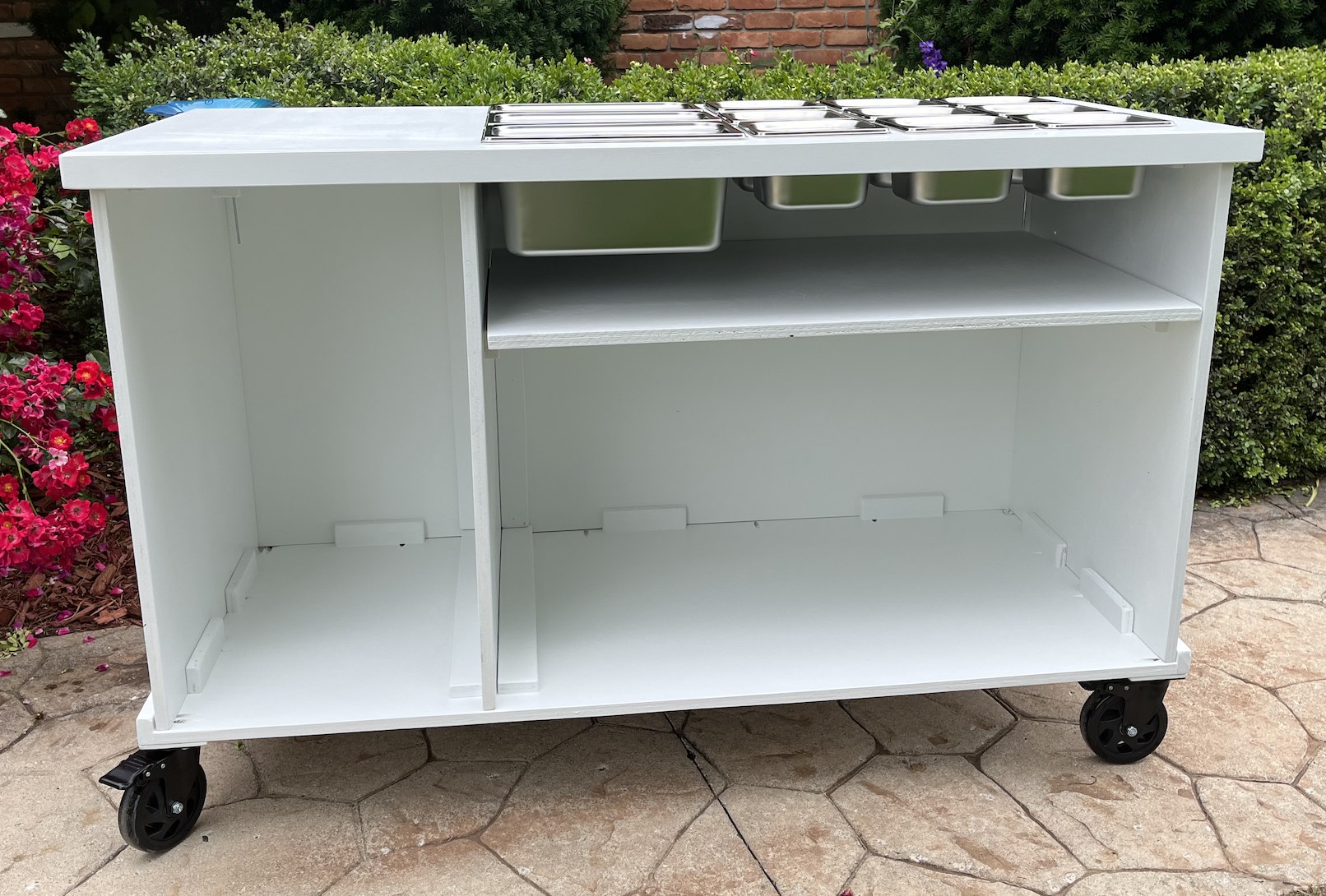 Grazing cart shown open: a clean white top with stainless wells and food containers, plus interior storage with a divider shelf