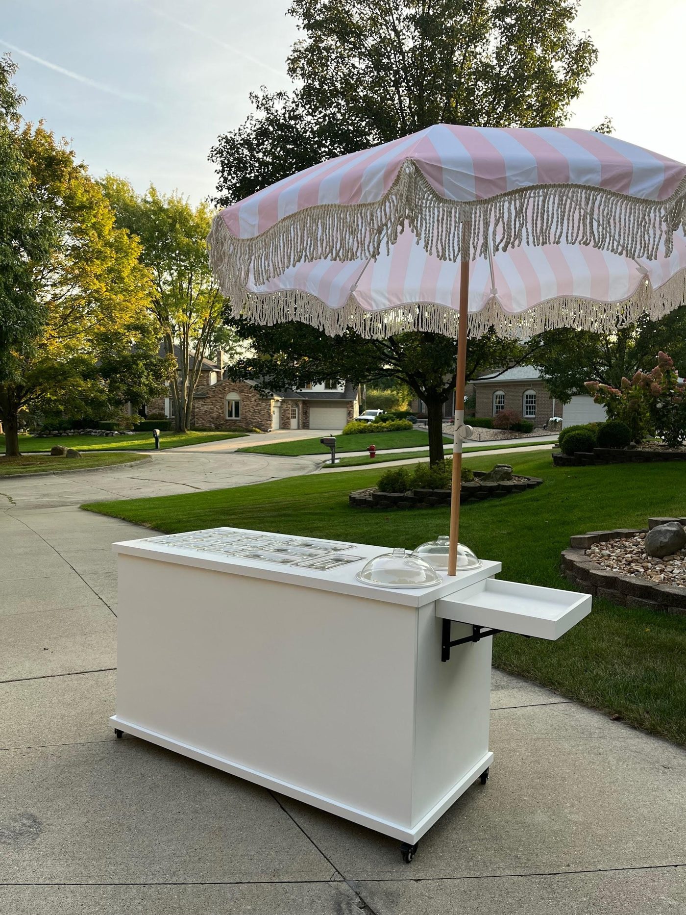 White ice cream and dessert cart with storage wells and a parasol umbrella, set up outdoors