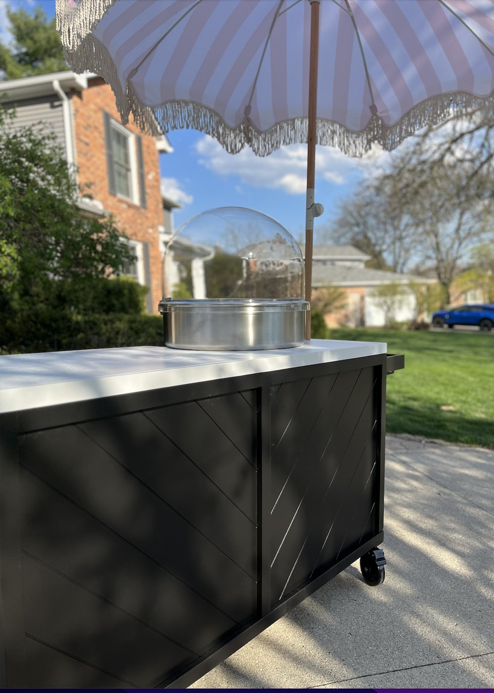 Black and white cotton candy cart with a chevron-pattern front and a pink-striped parasol